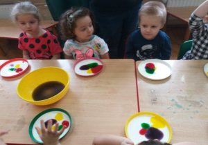 dzieci siedzą przy stolikach a na talerzach mleko a na nim kolorowe plamy